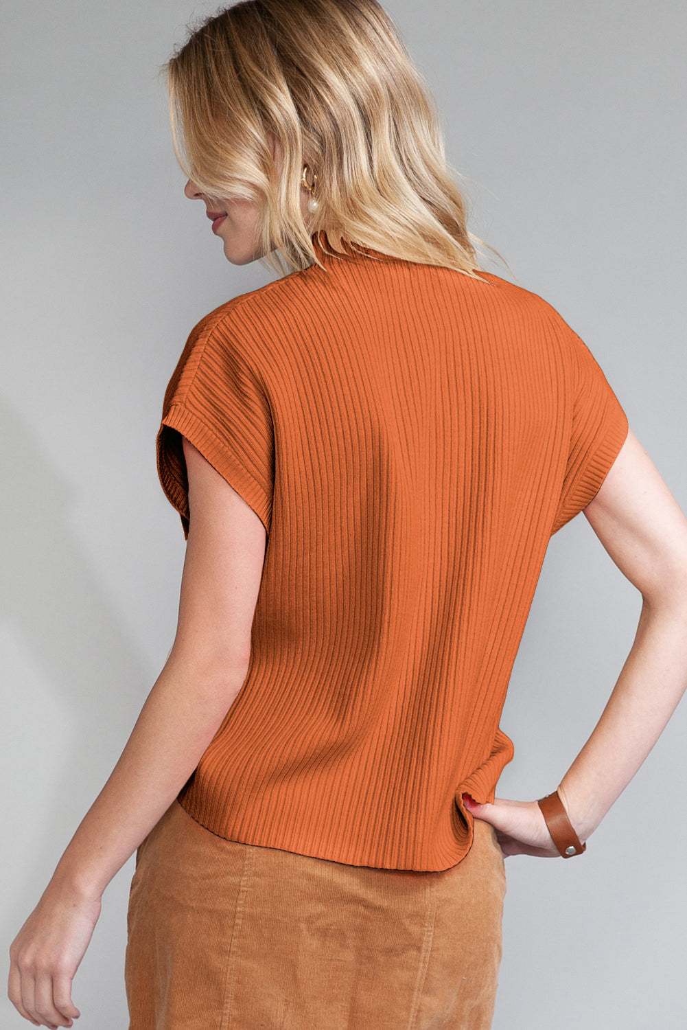 A blonde-haired individual wears a Shewin orange ribbed knit short sleeve sweater and a light brown skirt, seen from behind.