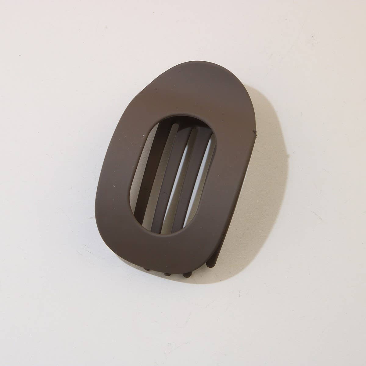 An ACCITY Oval Flat Hair Clip for Women with a brown matte finish and wide teeth rests on a white surface.