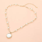 Round Pearl Pendant Station Necklace by Sensibling Corp., featuring a gold chain with evenly spaced pearls and a round white pendant, displayed on a light peach background. This elegant adjustable necklace blends timeless style with modern sophistication.