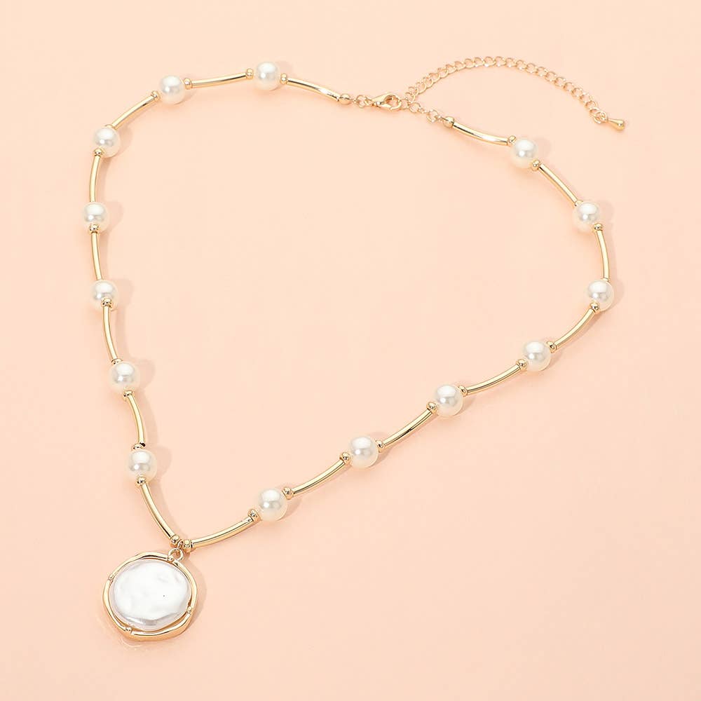 Round Pearl Pendant Station Necklace by Sensibling Corp., featuring a gold chain with evenly spaced pearls and a round white pendant, displayed on a light peach background. This elegant adjustable necklace blends timeless style with modern sophistication.