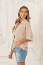 A woman stands sideways, smiling, wearing the Sew In Love Relaxed Fit Collared V Notch Neck Striped Top with rolled sleeves, paired with distressed denim shorts against an ornate white wall.