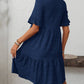 A woman models the Suhkasana Loose Casual Short-Sleeve Dress in navy blue, featuring a textured finish and ruffled hem, seen indoors from the back.