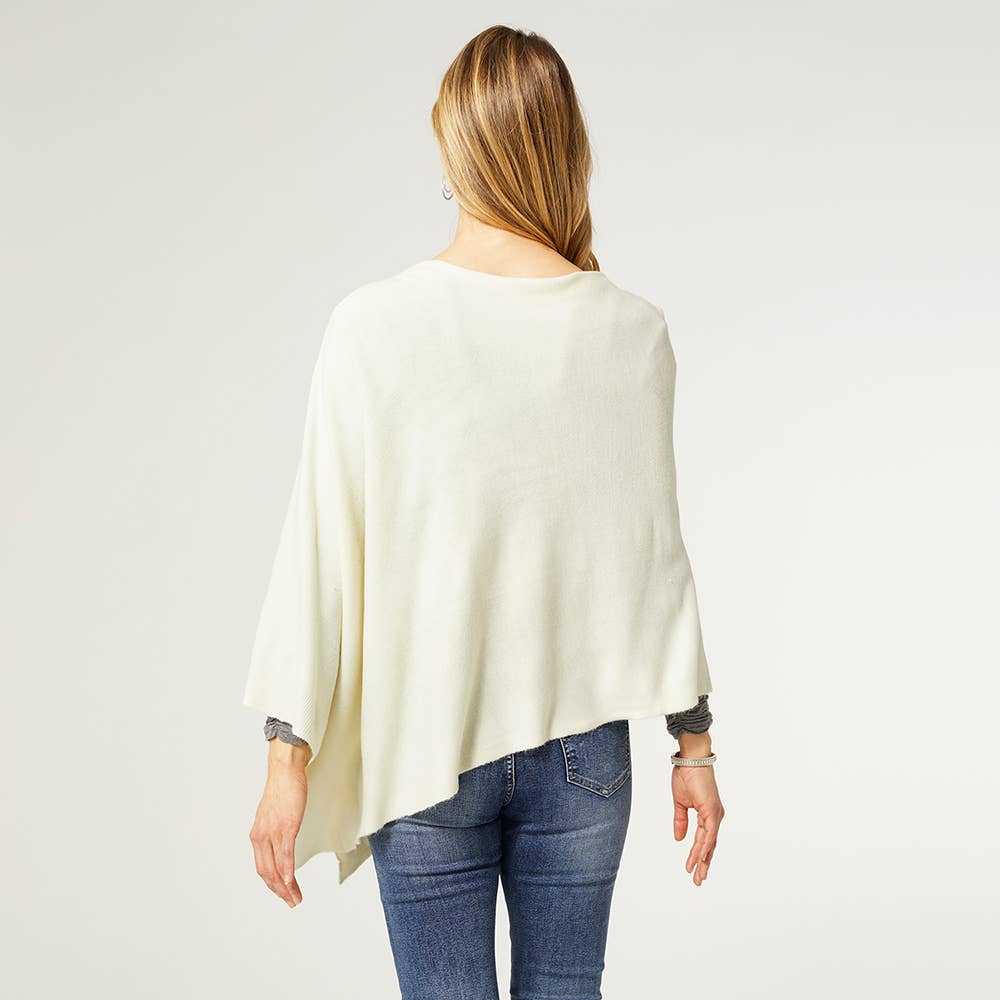 A person with long hair, seen from behind against a plain light background, models the COCO + CARMEN Lightweight Ponchos Wrap over blue jeans—creating an easy, stylish layered look.