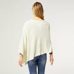 A person with long hair, seen from behind against a plain light background, models the COCO + CARMEN Lightweight Ponchos Wrap over blue jeans—creating an easy, stylish layered look.