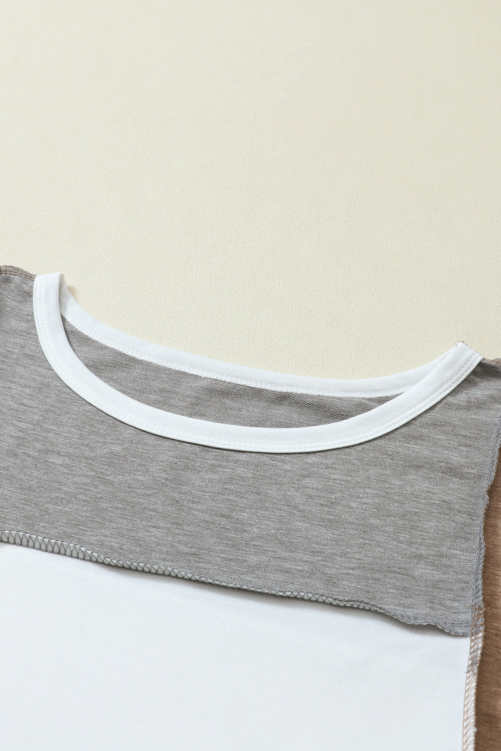 Close-up of the Shewin Khaki Color Block Exposed Seam Long Sleeve Top, highlighting its unique patchwork design in grey, white, and brown, with meticulous attention to stitching and neckline detail.