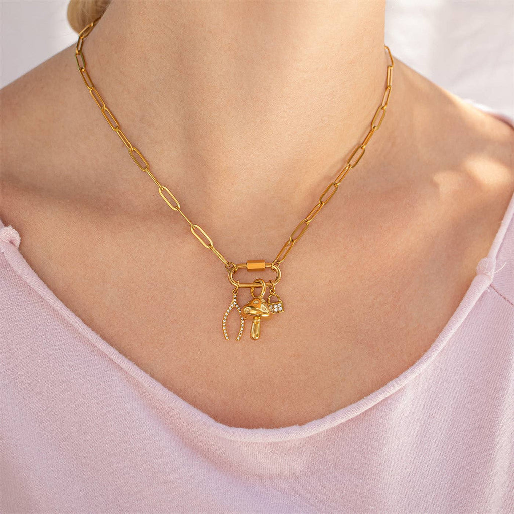 WJW's 18K Gold PVD Paperclip Carabiner Necklace, shown styled with three delicate gold and rhinestone charms and worn by a person in a light pink top, is a customizable piece that lets you elegantly display your favorite charms—perfect for adding sparkle to any outfit.