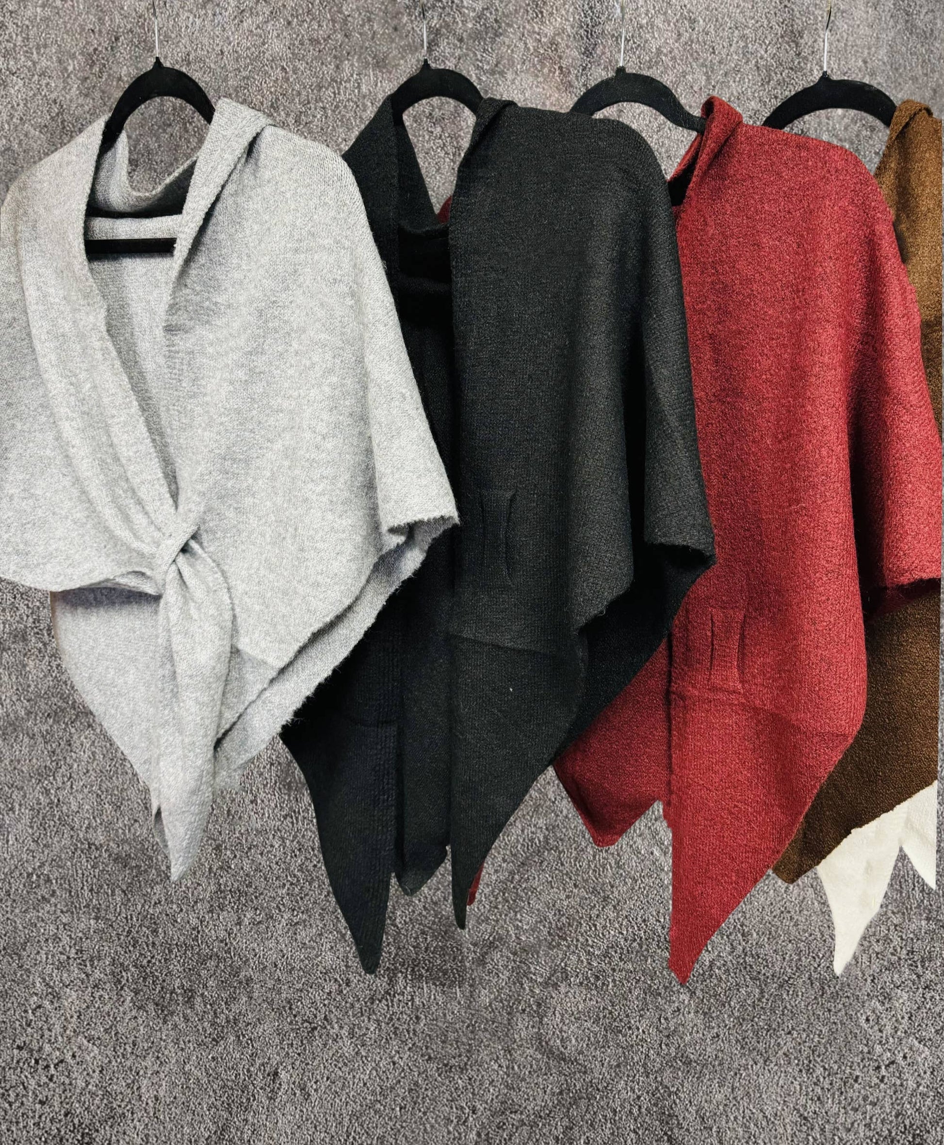 Four JC Sunny Fashion Cashmere-Blend Knit Triangle Shawls with cross-front design hang on black hangers in light gray, black, red, and brown against a textured gray background, featuring a chic oversized scarf-inspired look.