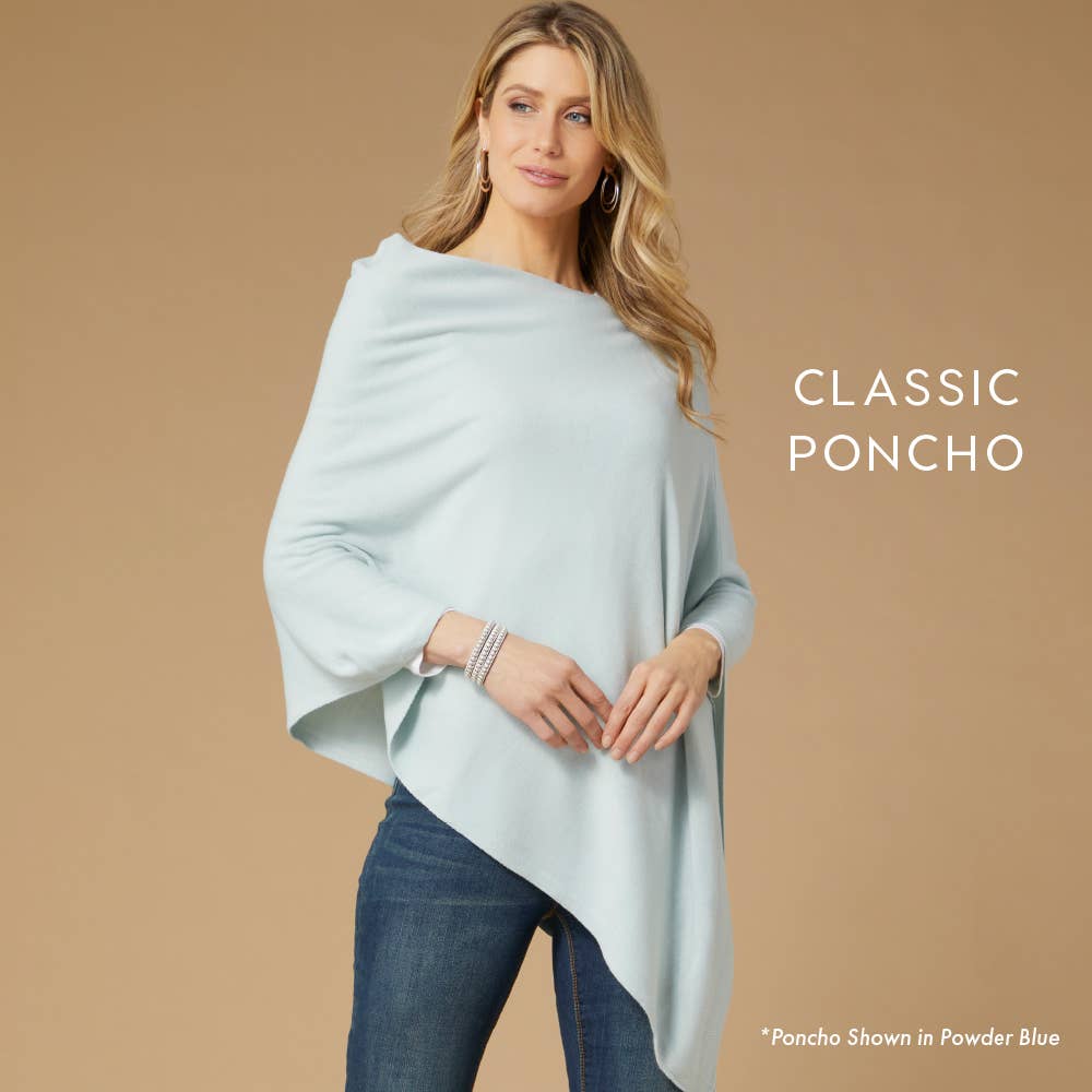 A woman in jeans wears the COCO + CARMEN Lightweight Ponchos Wrap in "Powder Blue" against a beige background. Text reads "Classic Poncho," emphasizing its versatility as a must-have layering piece.