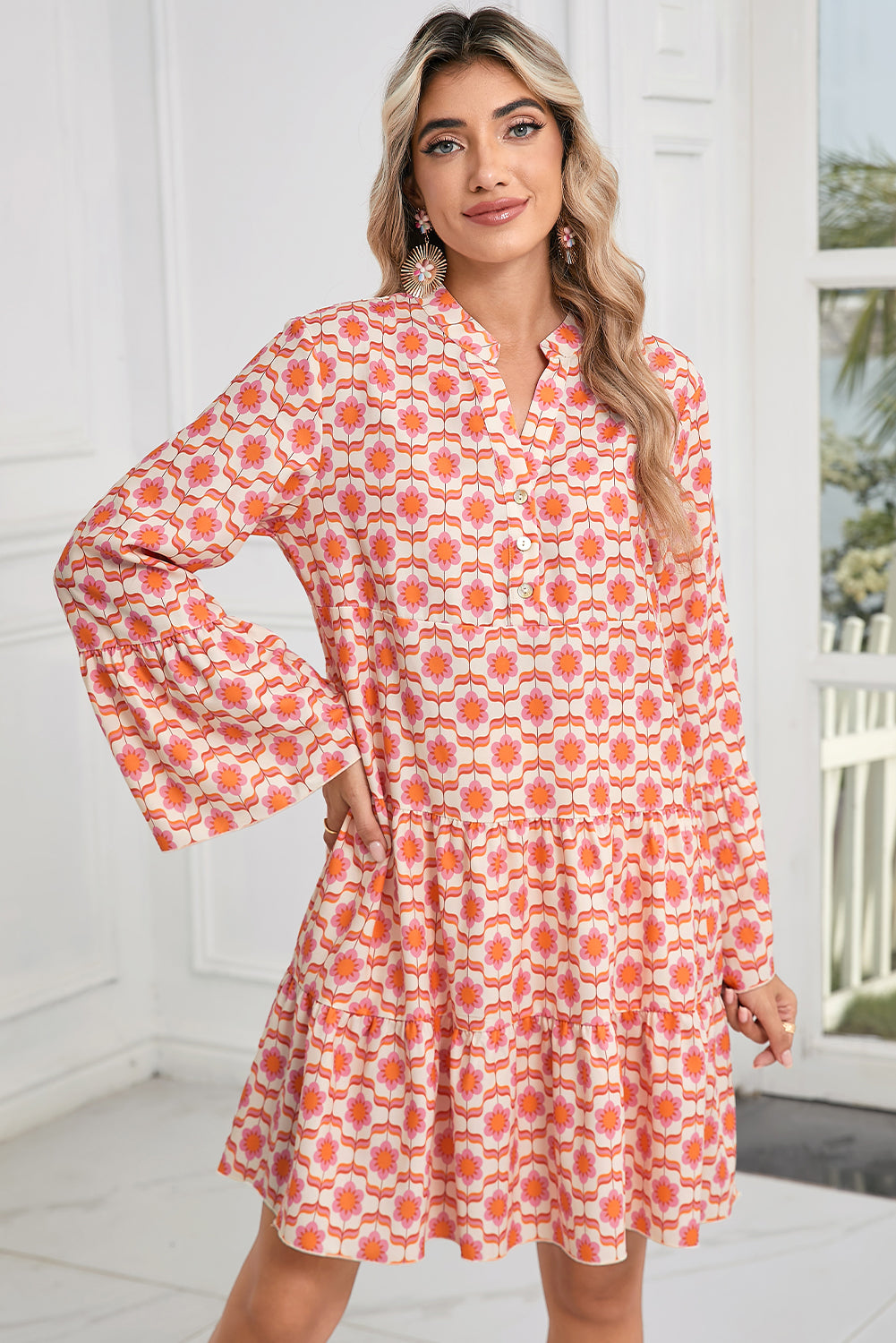 A woman indoors near a window and door wears the Shewin Orange Floral Button V Neck Bell Sleeve Mini Dress.