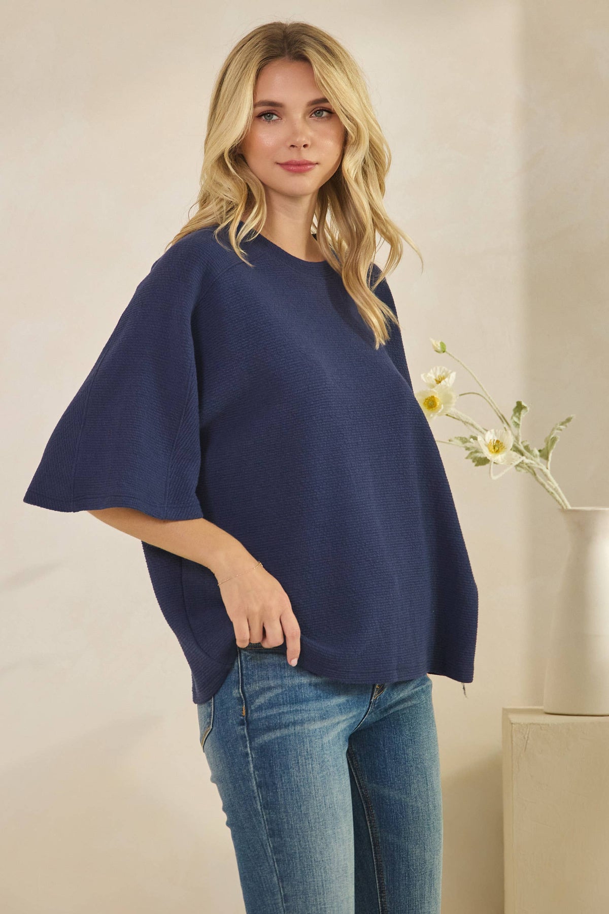 A woman wearing a dark blue, 3/4 sleeve CLOUDY KNIT 3/4 SLEEVE ROUND NECK TOP with a round neck and blue jeans.