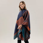 A woman is wearing the ACCITY SHAWL SCARF FAUX CASHMERE SLIT CAPE in a navy blue and orange pattern, styled as a blanket scarf, standing against a plain light gray background.