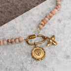 The WJW Stainless Steel Chunky Glass Bead Carabiner Necklace features a gold-toned clasp, accented with a round bee-design charm and a small gold bee charm, displayed on a textured surface.