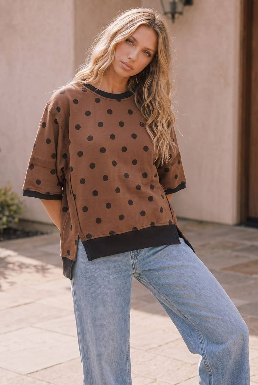 A woman wearing a Kori America Mocha Polka Dot Oversized Top with black trim at the sleeves and hem, paired with light blue jeans.