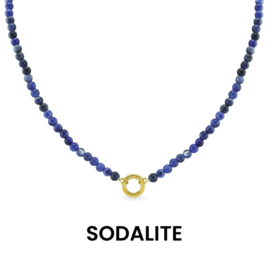 A Semi Precious Natural Stone Charm Keeper Necklace by WJW, featuring round blue sodalite beads and a central 18K Gold PVD Coated clasp, is displayed against a white background. Below the necklace, the word "SODALITE" appears.