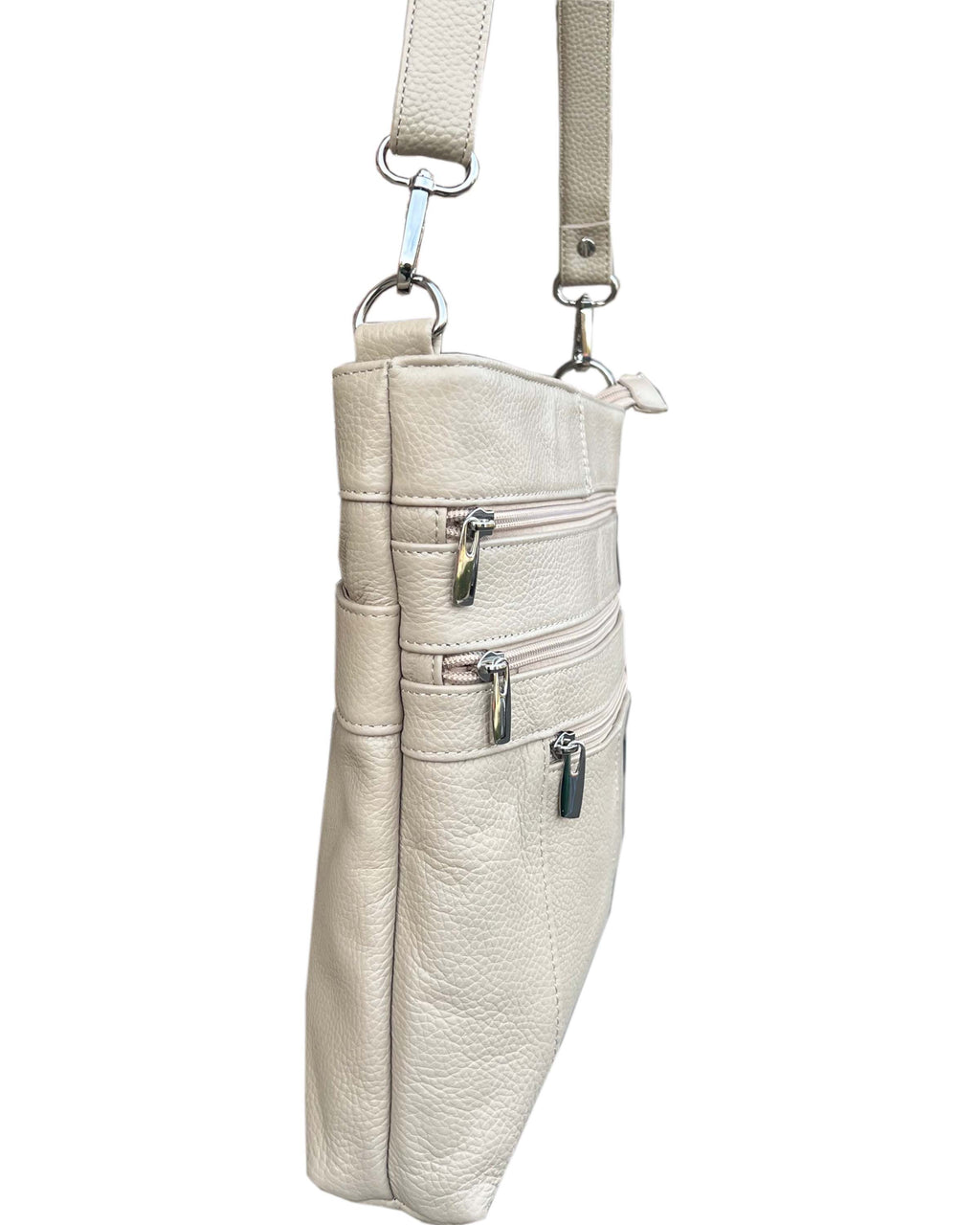 A side view of the Roma Leathers, Inc. cowhide leather crossbody bag shows its light beige color, three exterior zippered pockets, and adjustable strap.