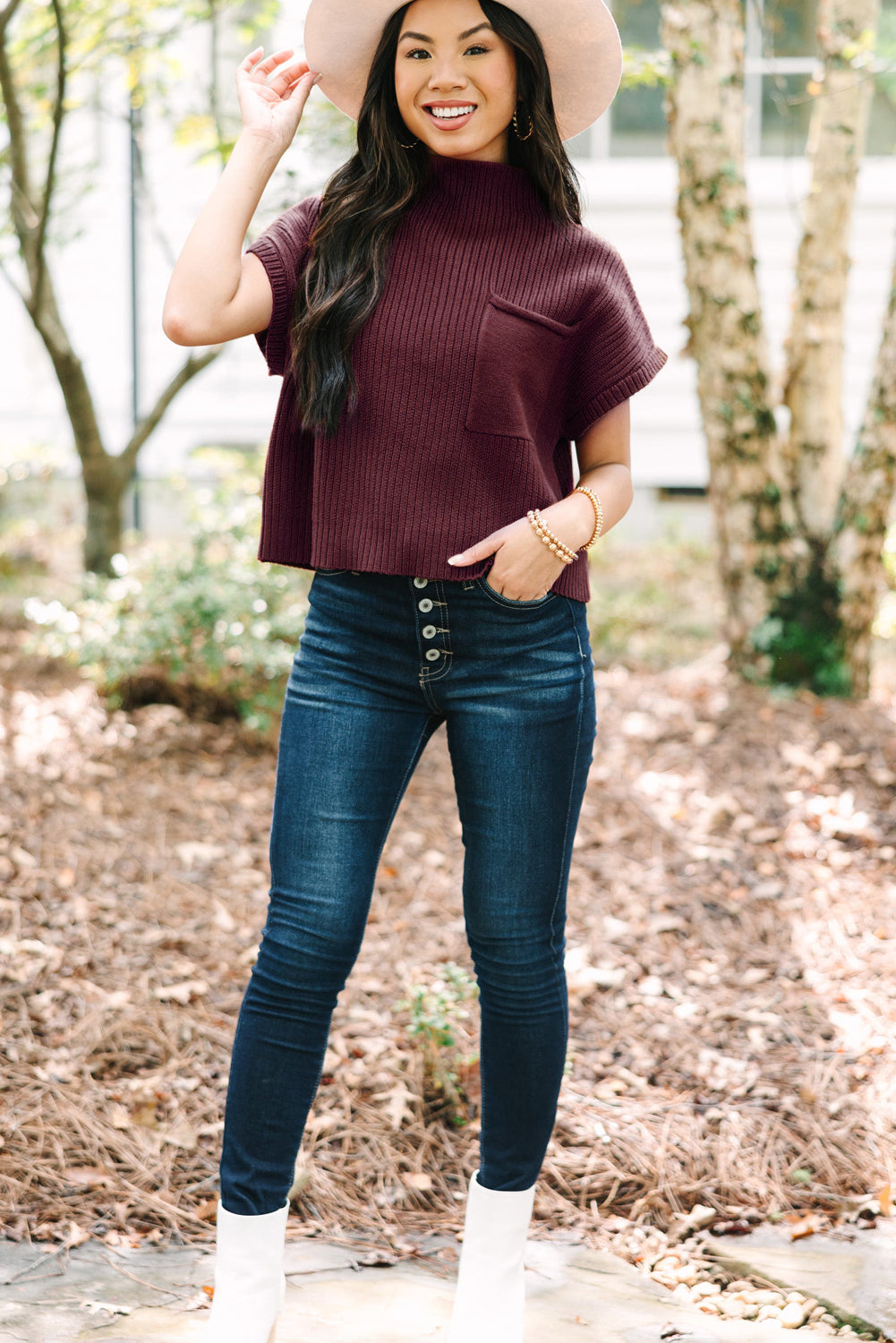 A woman poses outdoors in a Patch Pocket Ribbed Knit Short Sleeve Sweater by Shewin, paired with jeans, a beige hat, and white boots, highlighting her casual style for transitional weather.