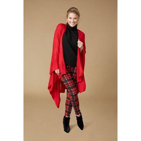 A woman wearing the COCO + CARMEN Kiara Lightweight Wrap over a black turtleneck, red plaid pants, and black boots stands against a plain beige background.