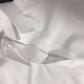 A close-up of the Rosa Clothing White Relaxed Short Sleeve Blouse with a visible tag, laid flat on a gray surface.