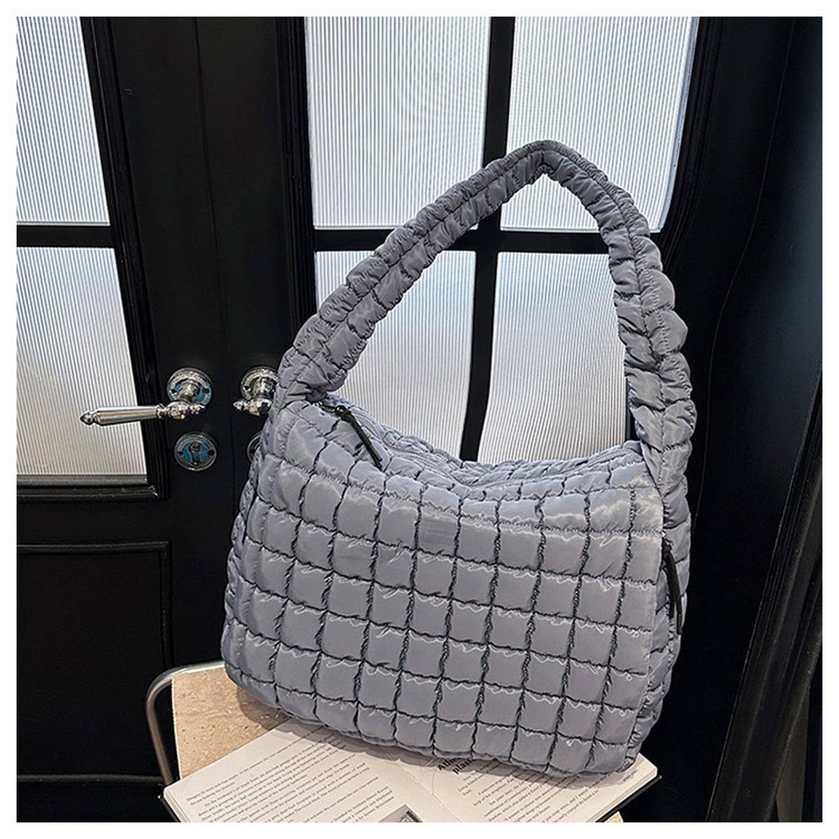 The ACCITY Cloud Tote Bag Large Shoulder Crossbody—a stylish gray pleated nylon bag with a thick padded handle—sits on a chair by some papers, ideal for modern women seeking trendy fashion and functionality.