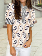 A woman wears the 1 the Woman Floral Striped Patchwork Button Neck Short Sleeve Blouse with white pants while standing outdoors.