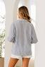 A woman with long hair faces away indoors by arched openings, wearing the Sew In Love Relaxed Fit Collared V Notch Neck Striped Top and white frayed shorts.
