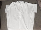 A White Relaxed Fit Short Sleeve Blouse from FASHION GO is laid flat on a grey surface, highlighting its crisp button-up design and casual silhouette, with a tag attached.