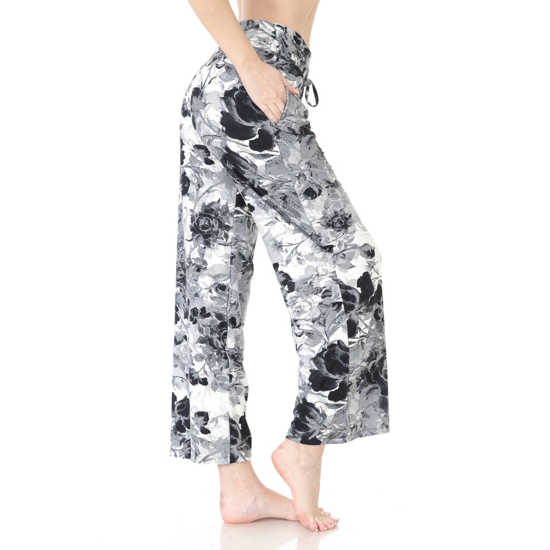 A person stands barefoot against a white background wearing Leggings Depot Buttery Soft Print Pajama Pants—loose-fitting, high-waisted, black and white floral print with an elastic waistband and pockets. Main image