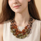 A woman wearing a cream sleeveless top and a statement jewelry piece—a Sensibling Corp. Chunky Beaded Layered Statement Necklace adorned with oversized beads in rich brown, green, and amber hues.