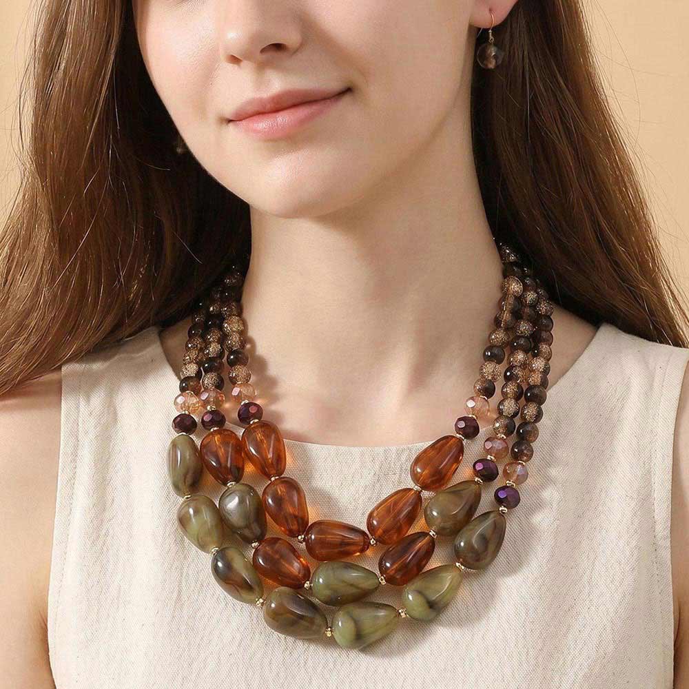 A woman wearing a cream sleeveless top and a statement jewelry piece—a Sensibling Corp. Chunky Beaded Layered Statement Necklace adorned with oversized beads in rich brown, green, and amber hues.