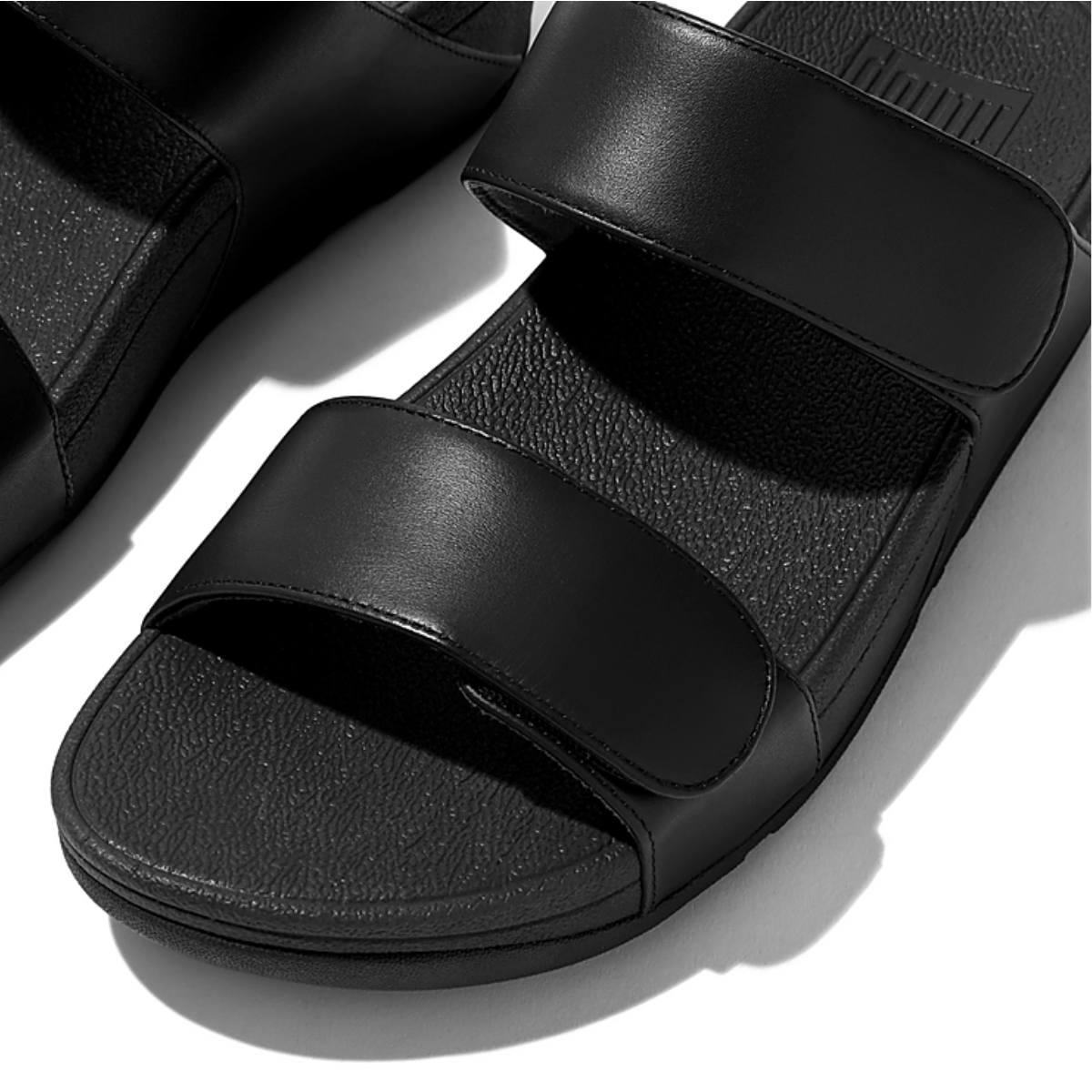 A pair of Lulu Adjustable Leather slide in Black sandals from Flipflops & Whatnots providing exceptional comfort, resting on a pristine white surface.