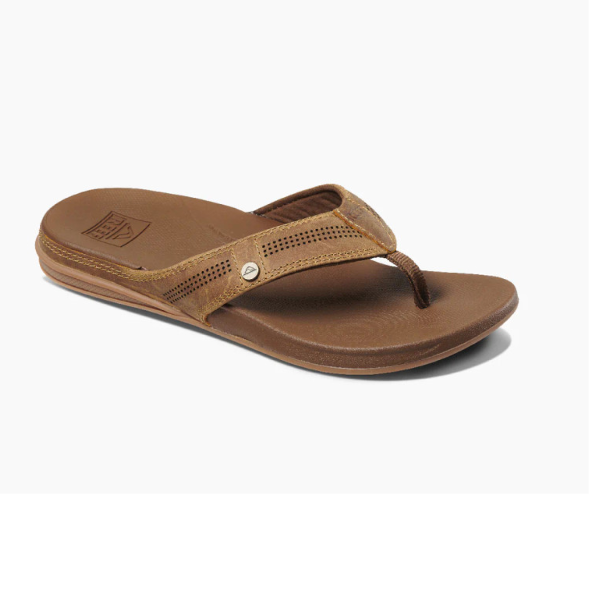 The REEF Cushion Lux in Toffee is a men's sandal featuring a brown flip-flop design with full-grain leather perforated straps and a small metallic stud on one side, shown against a white background.