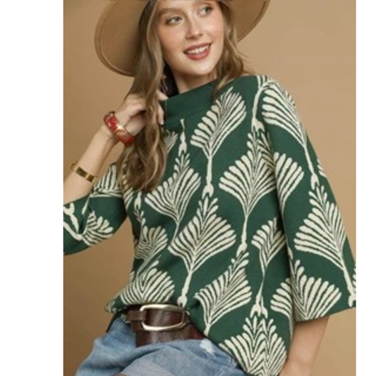 A woman models the Abstract Print Pullover Sweater in Forest Green by Umgee, styled with jeans, bracelets, and a belt, topped with a wide-brim hat—an ideal look for fall layering against a beige backdrop.