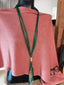 A mannequin draped in a pink fabric displays the Multi Row Green Tassel Long Necklace Set by SPECIAL EFFECTS, featuring multiple green strands with a gold accent, elegantly hanging down.