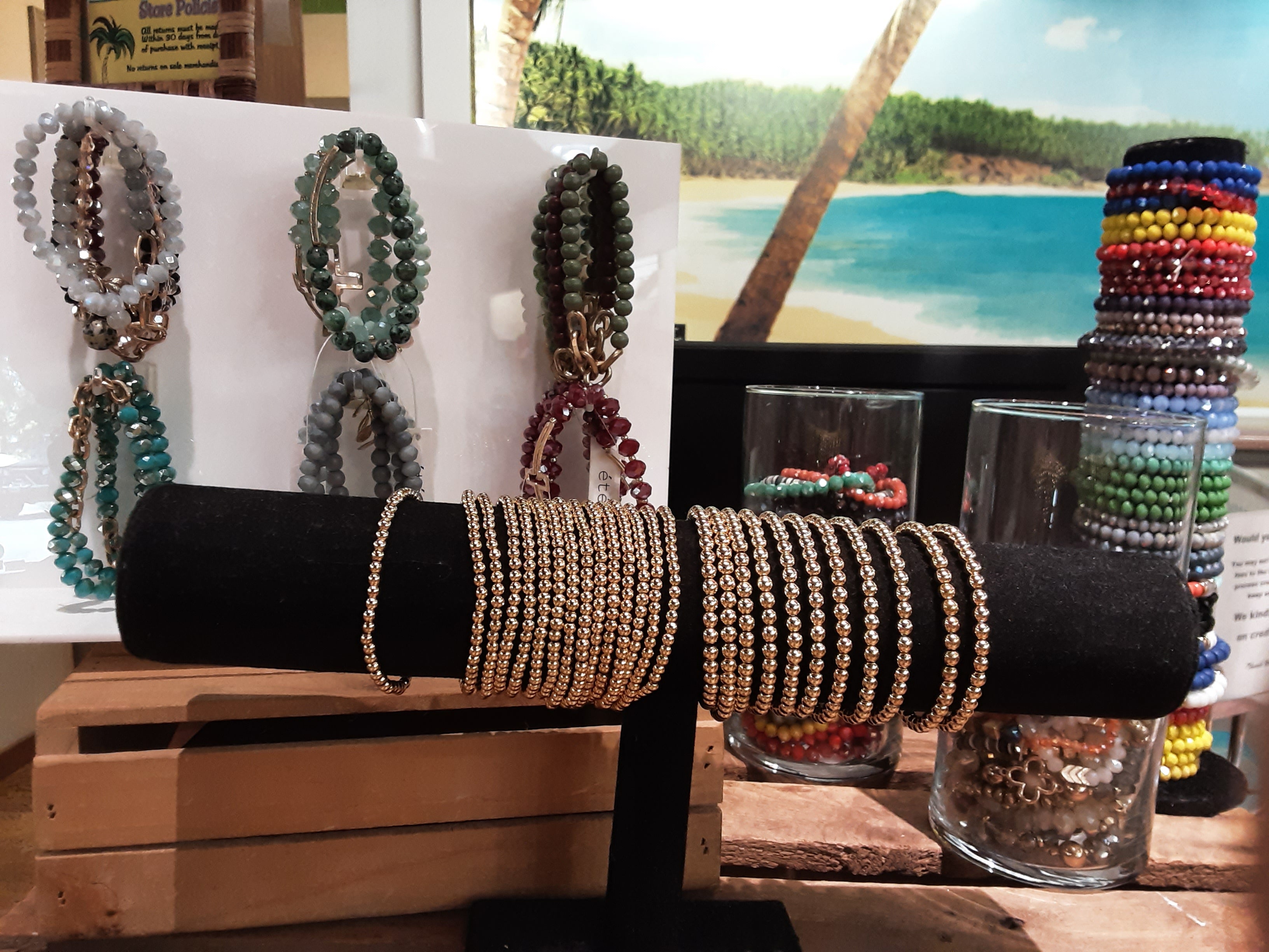 FASHION GO's 5 for $35 BRACELET ASSORTED set features colorful, textured beaded and metallic elastic bracelets, displayed on stands and in glasses with a beach scene photo in the background.