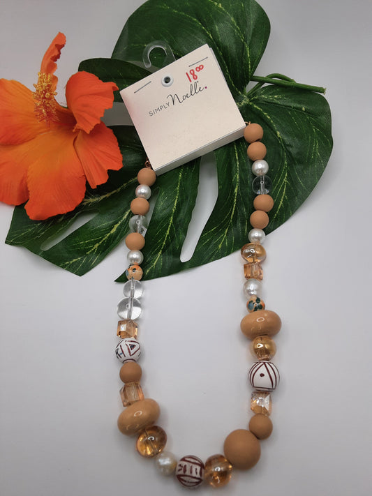 The SIMPLY NOELLE SNECK 100 ASST by Ganz Inc is a beaded necklace featuring assorted brown, white, and clear beads, displayed against green leaves and an orange hibiscus flower. The price tag reads "$18.00".