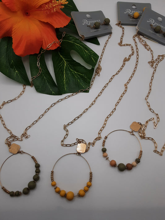 A PROJECT 3957 WOOD necklaces with circular bead pendants and matching earrings by SPECIAL EFFECTS, displayed on a white background alongside orange flowers and green leaves.