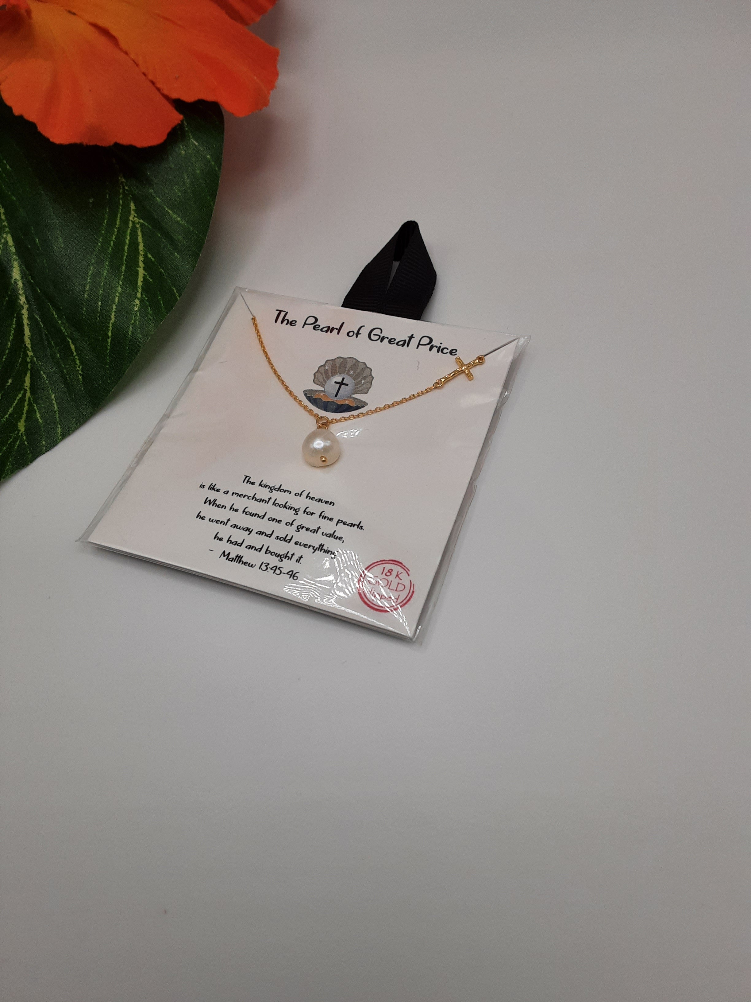The "Pearl of Great Price 16 inch Necklace" by SPECIAL EFFECTS is elegantly displayed on a card adorned with religious text, featuring a cross and a pearl. The card is topped with a black ribbon, while an orange flower and green leaf are visible on the left side. Main image