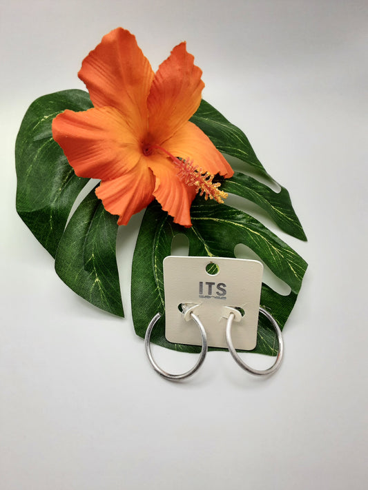 A pair of earrings labeled "ITS E6562 ASSORTED" by Fashion Go, displayed on a white card, is placed on top of a large green leaf alongside an orange hibiscus flower.