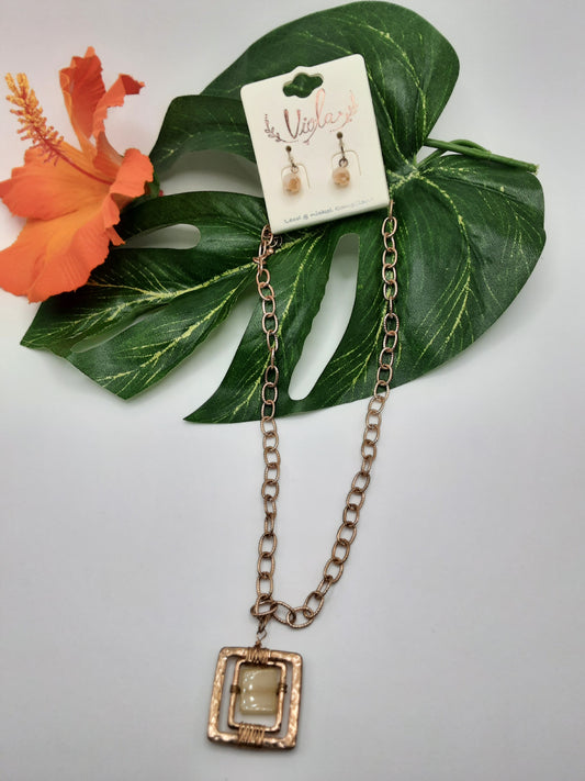 The VIOLA 6493 SQUARE gold necklace and matching earrings by SPECIAL EFFECTS are displayed on a white background, adorned with green leaves and an orange hibiscus flower.