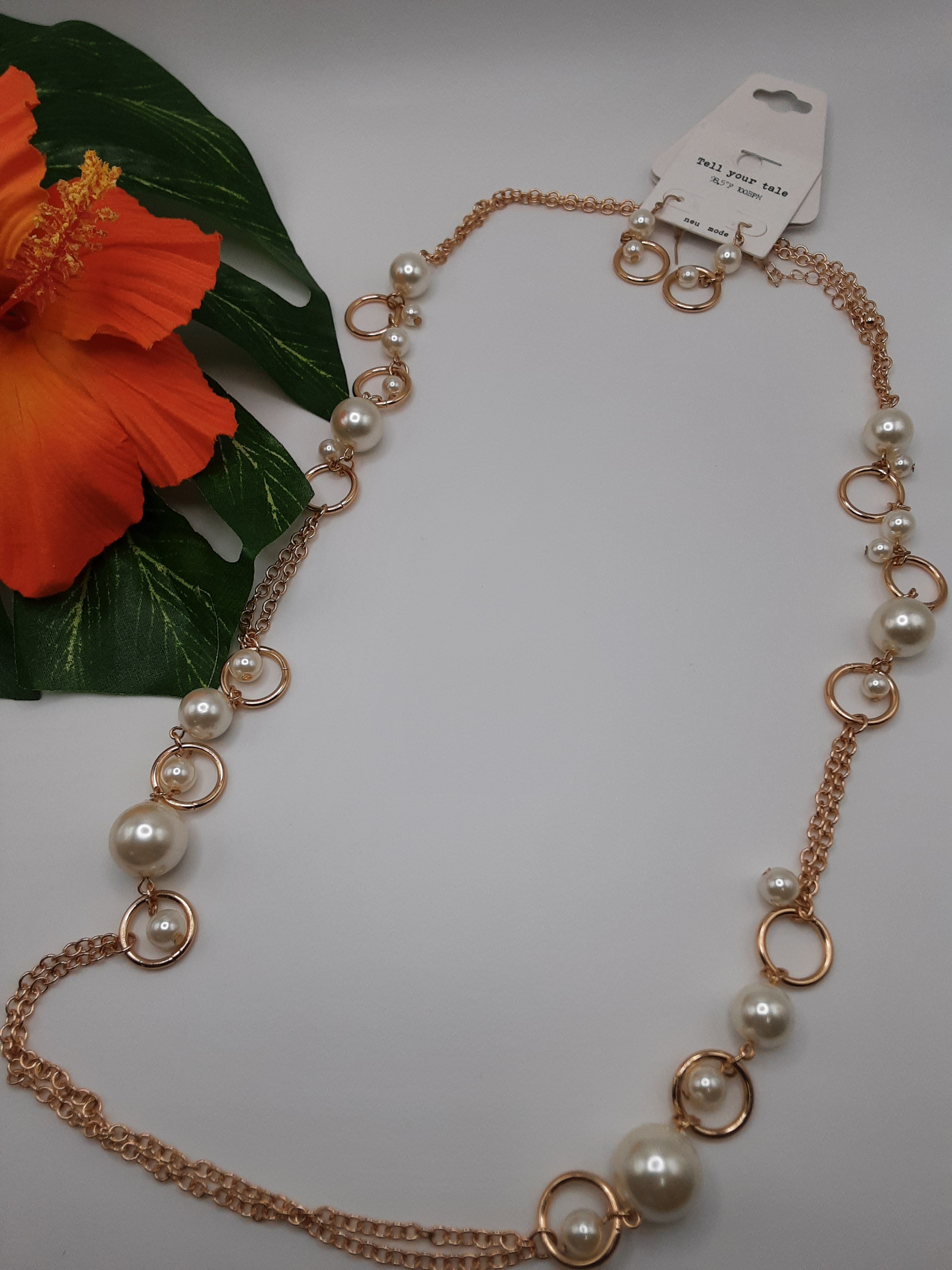 The 36" CHAIN W/PEARLS SET by SPECIAL EFFECTS features gold rings and pearl-like beads. It's visually enhanced with an orange hibiscus flower resting on a green leaf nearby. The tagged necklace is elegantly arranged against a white background. Main image
