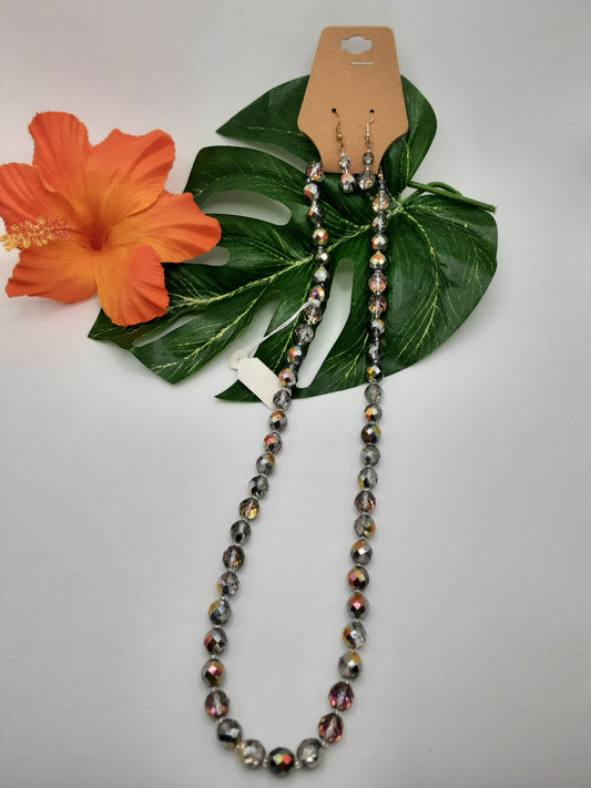 Special Effects 18054 Crystal necklace and earrings set displayed against a green leaf with an orange flower on the side.