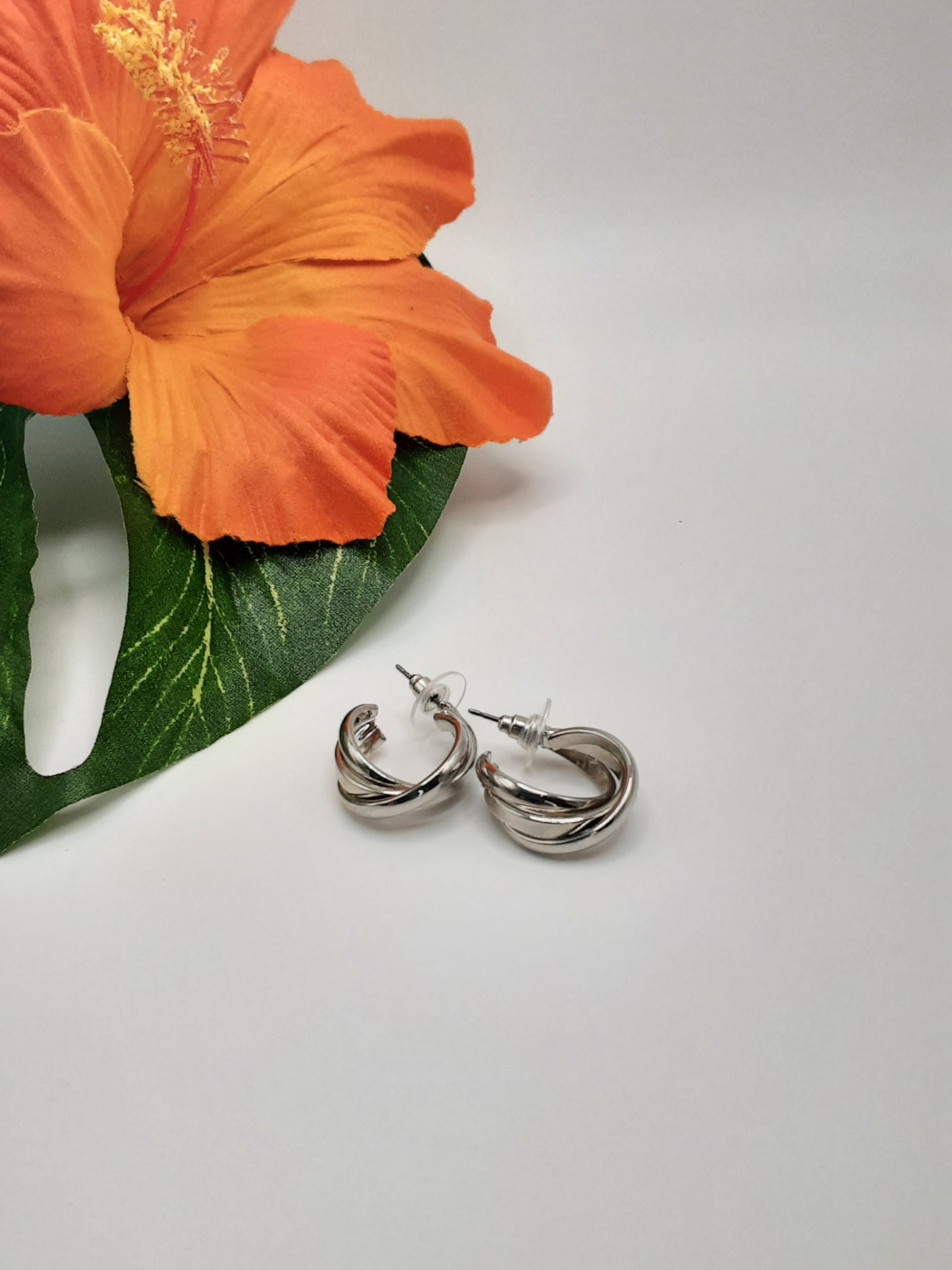 A pair of CITY 9761 MULTI earrings by SPECIAL EFFECTS is placed on a white surface next to an orange hibiscus flower.