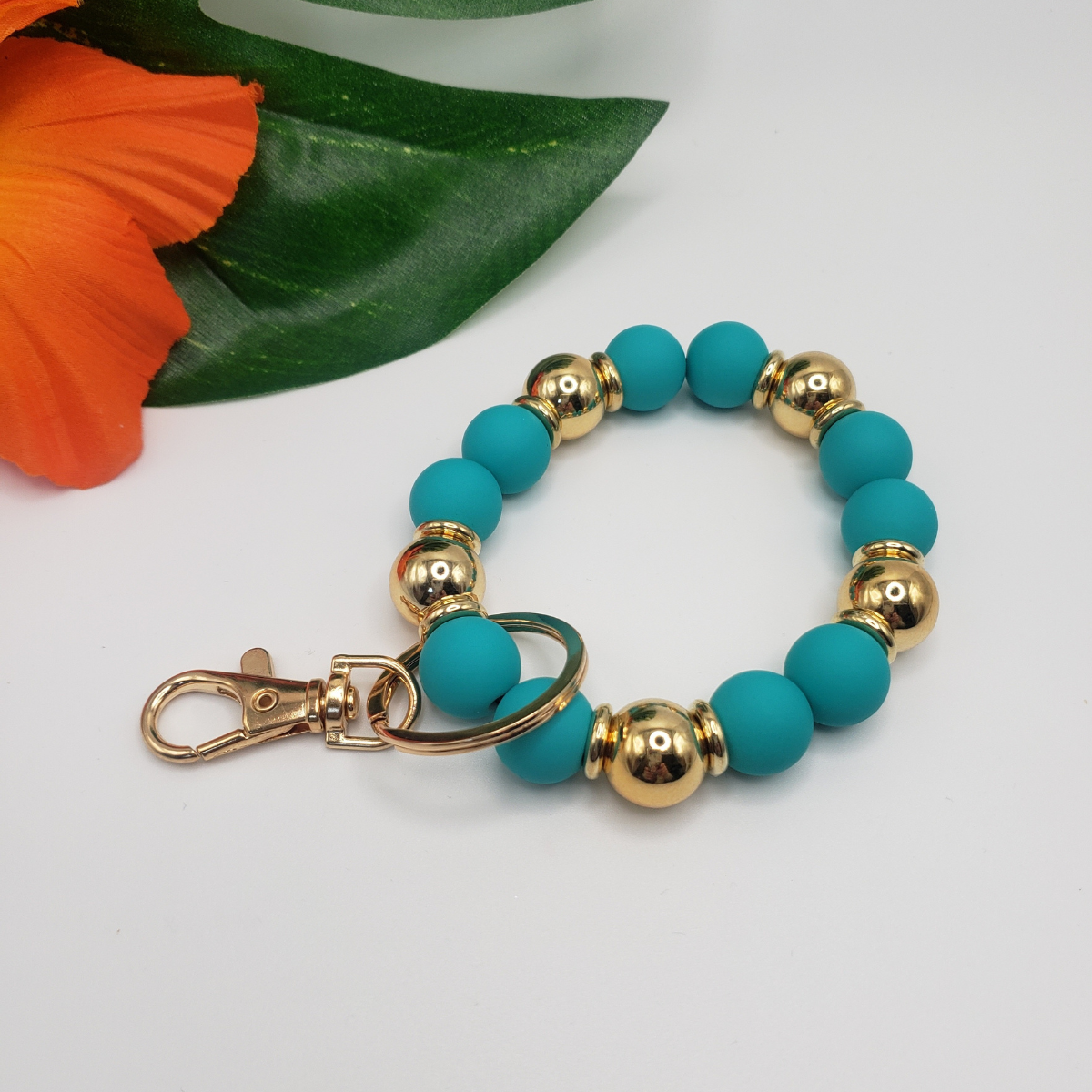 A Gold and Color Bead KeyChain by Ganz Inc with a flower in the background.