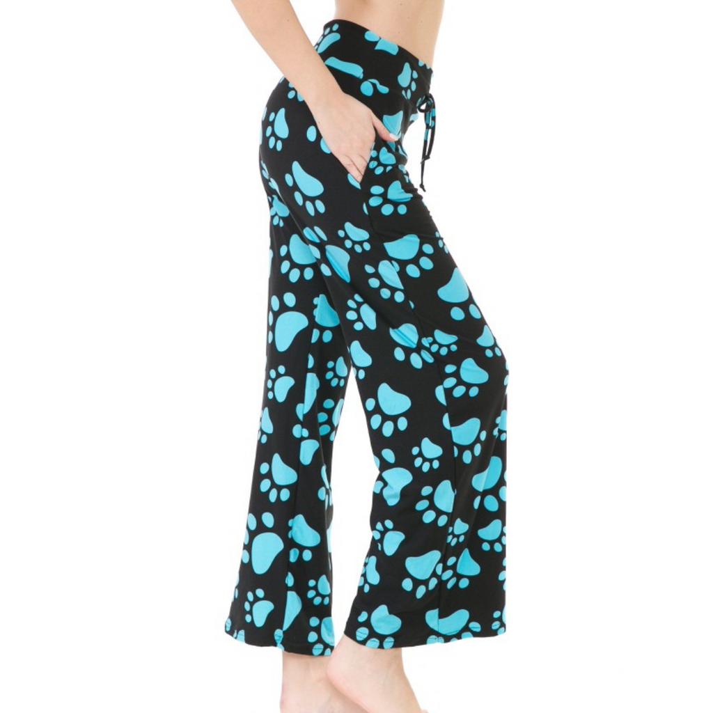Side view of a person wearing FASHION GO's Buttery Soft Pajama Pants with Drawstring adorned with blue paw print patterns, featuring an elastic waistband and functional pockets. Their right hand is in the pocket, and they are standing barefoot.