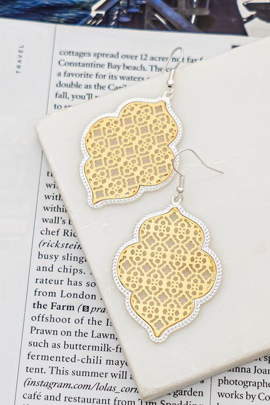 A pair of high-quality FASHION GO Two Tone Openwork Brass Stamping Earrings resting on an open magazine page.