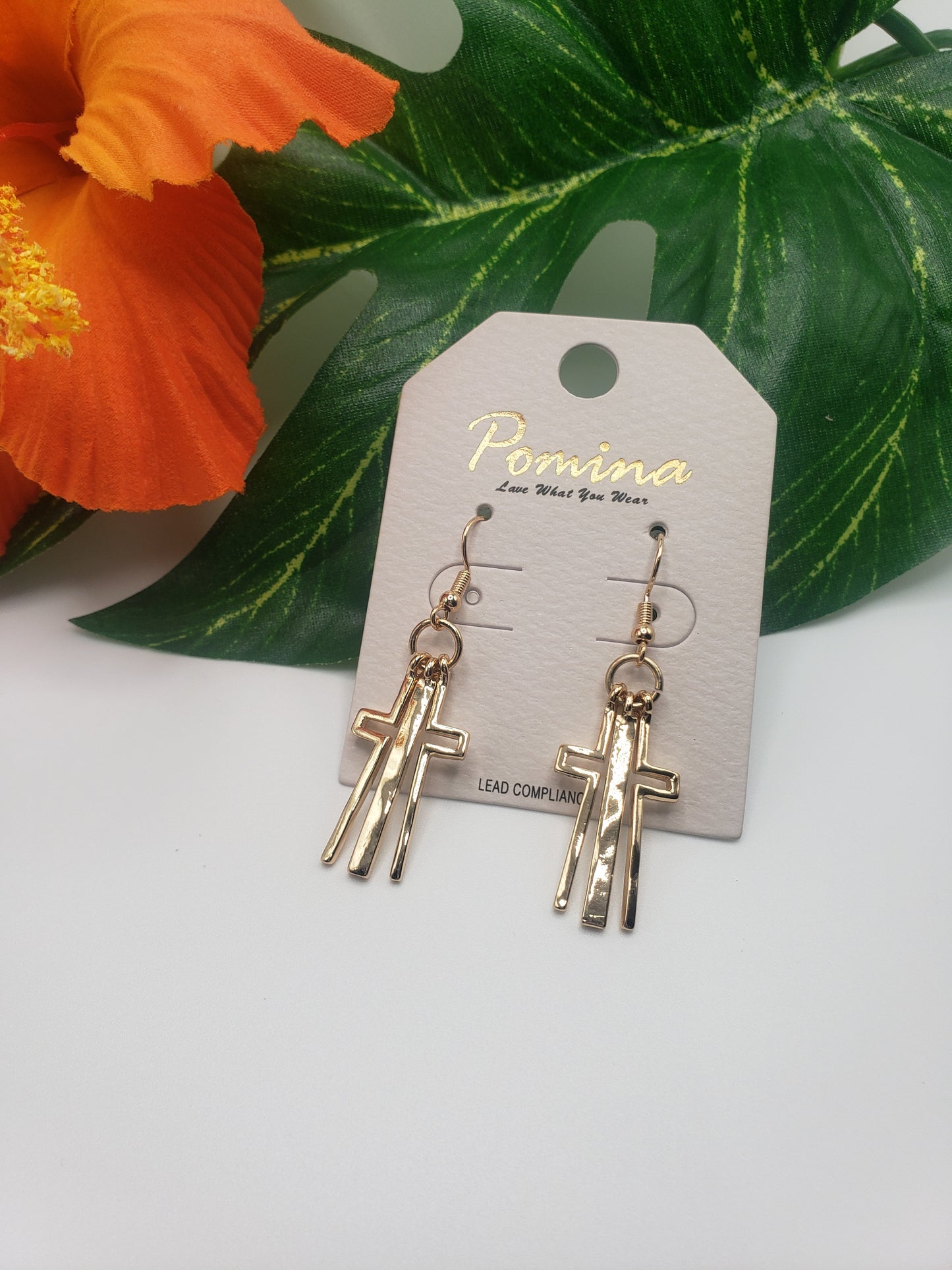 A pair of Fashion Go CROSS EARRING in gold with a flower in the background.