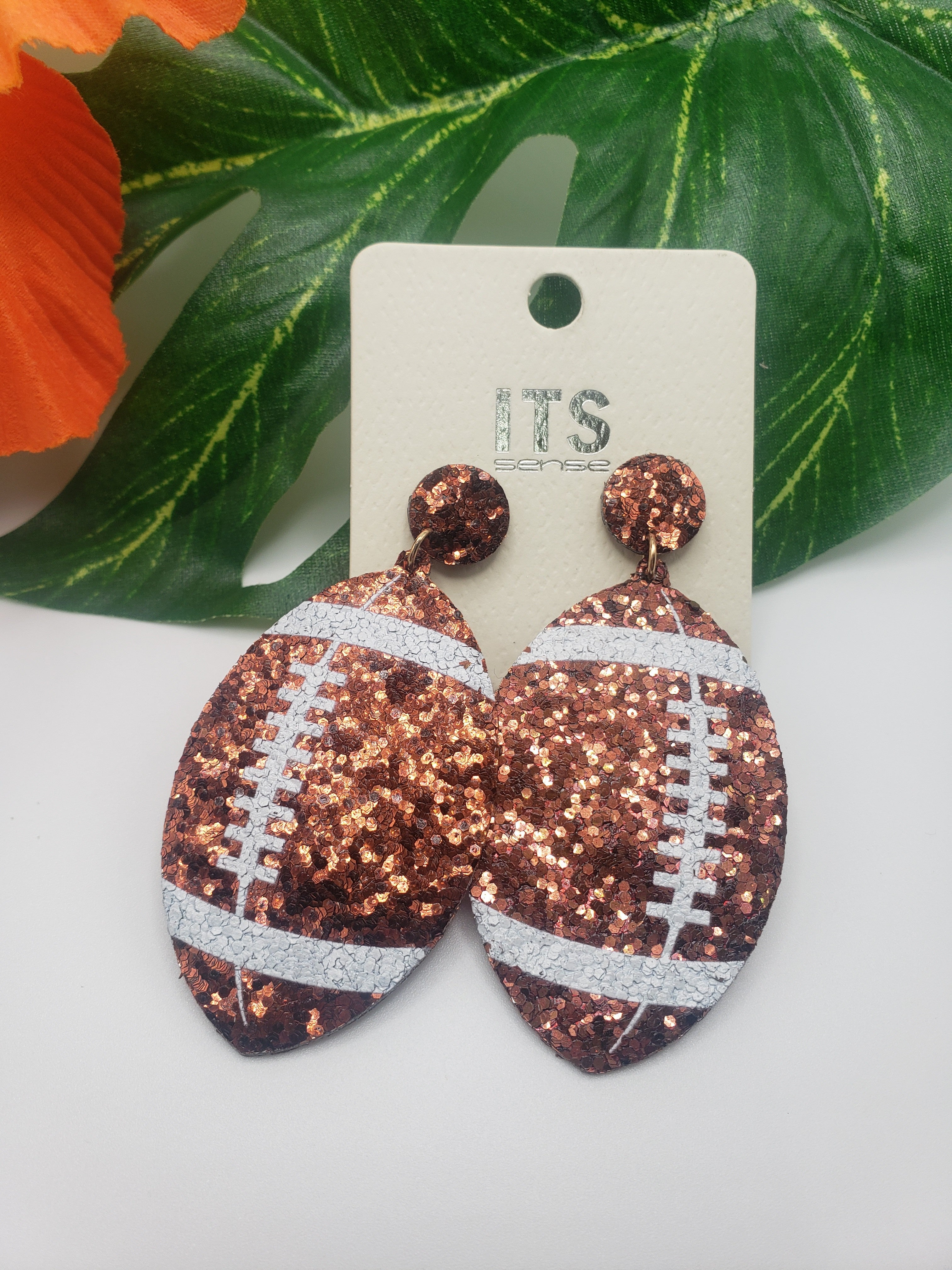 A pair of SPECIAL EFFECTS Football glitter earrings with silver and copper tones displayed on a white earring card, embodying team spirit. Main image