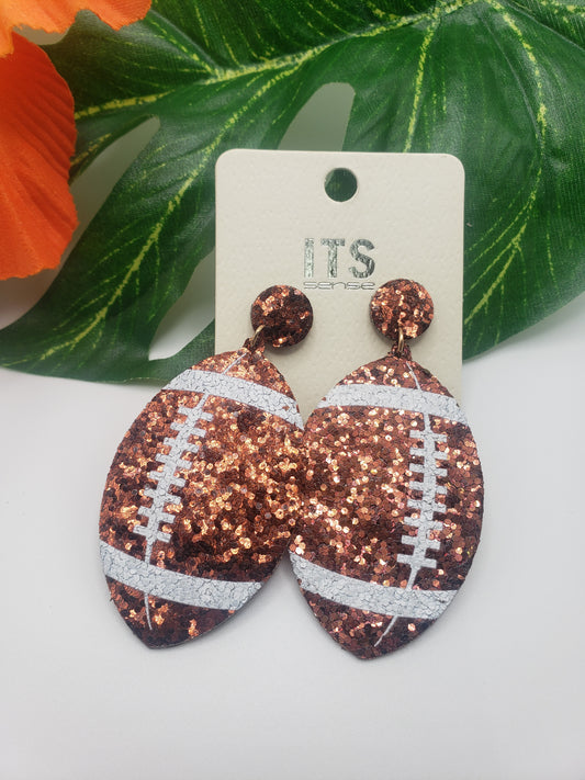 A pair of SPECIAL EFFECTS Football glitter earrings with silver and copper tones displayed on a white earring card, embodying team spirit.