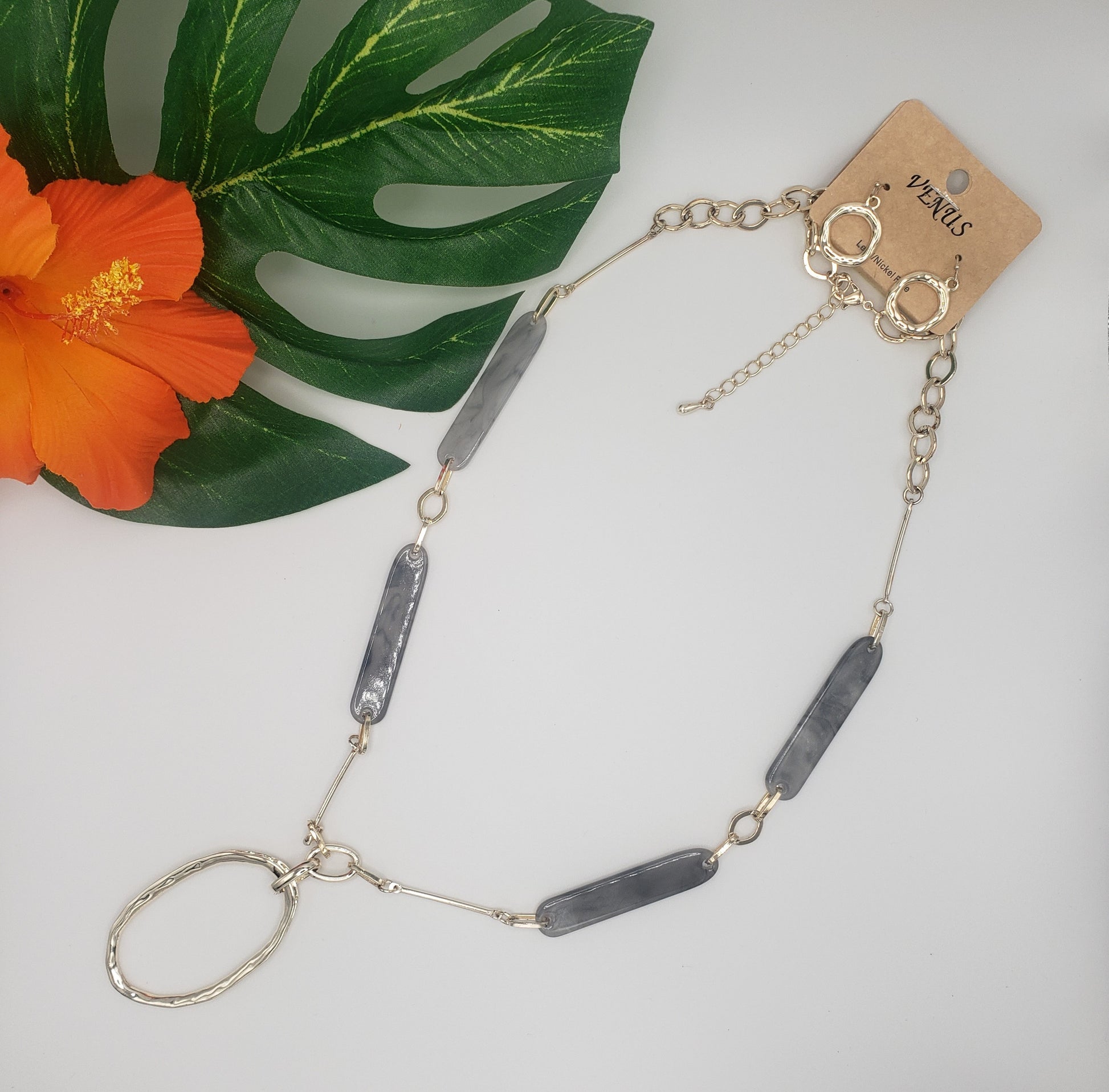 Grey and Gold Station Necklace w/Earrings displayed next to a tropical leaf and a gold-tone pendant.