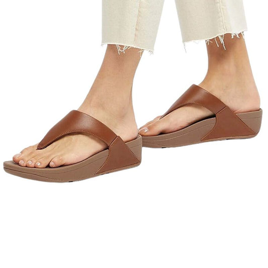 A pair of FITFLOP LULU LEATHER LIGHT TAN FLIP FLOPS worn with frayed-hem jeans.